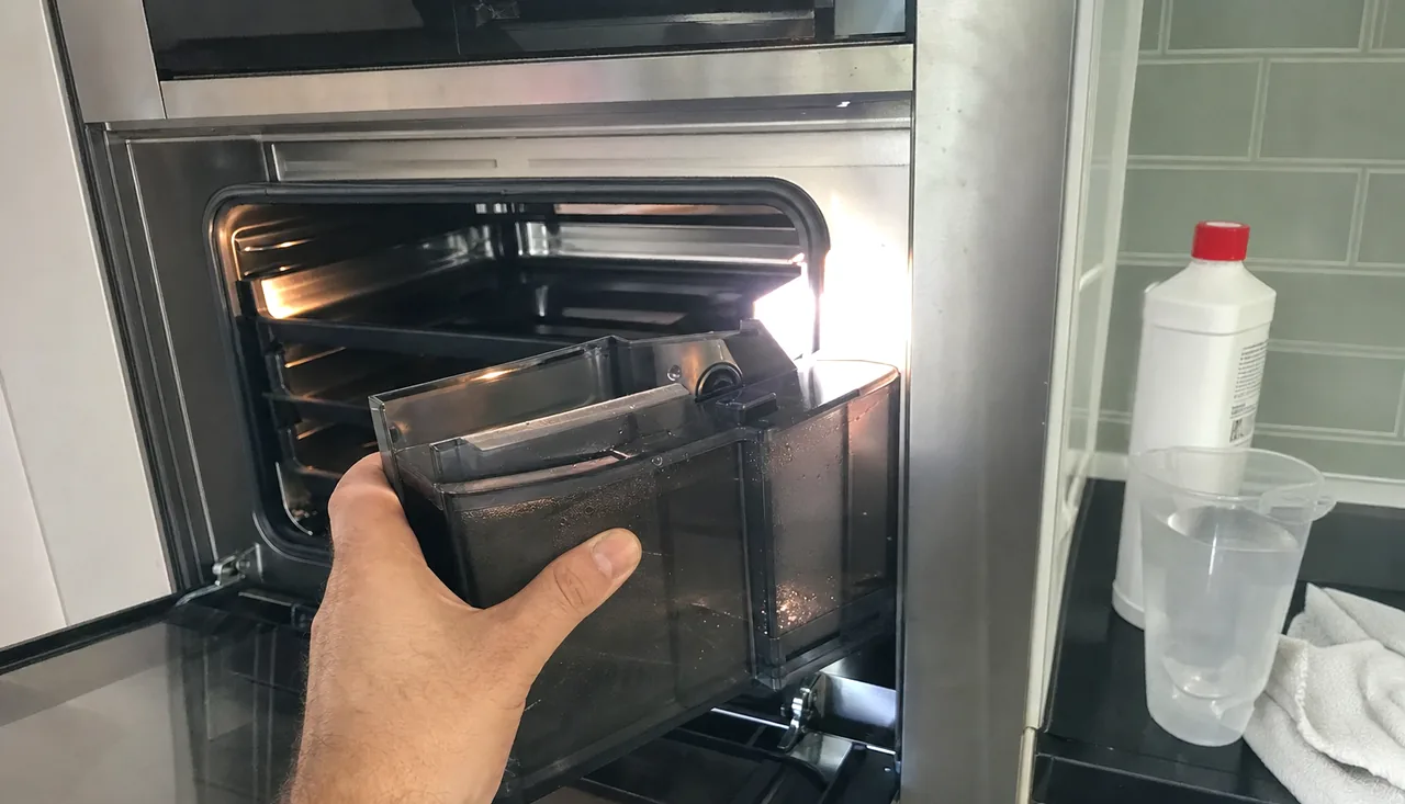 Descaling solution and a plastic measuring beaker standing on a counter beside an open steam oven