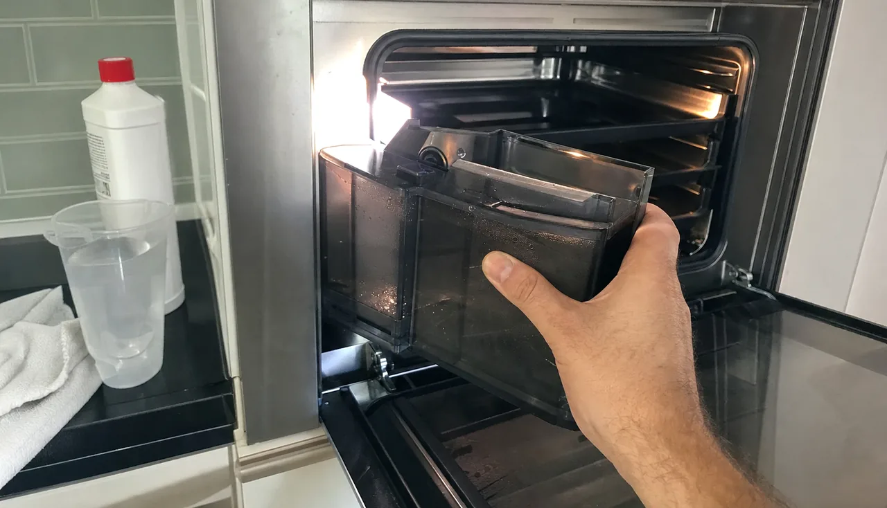 A built-in steam oven open at eye level, the reservoir in one hand, an ordinary kitchen counter to the side