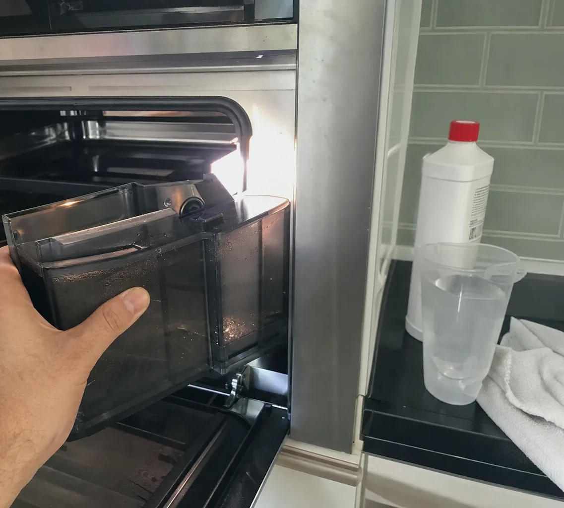 A close view of a steam oven water tank in a hand, the cavity light catching the condensation on it