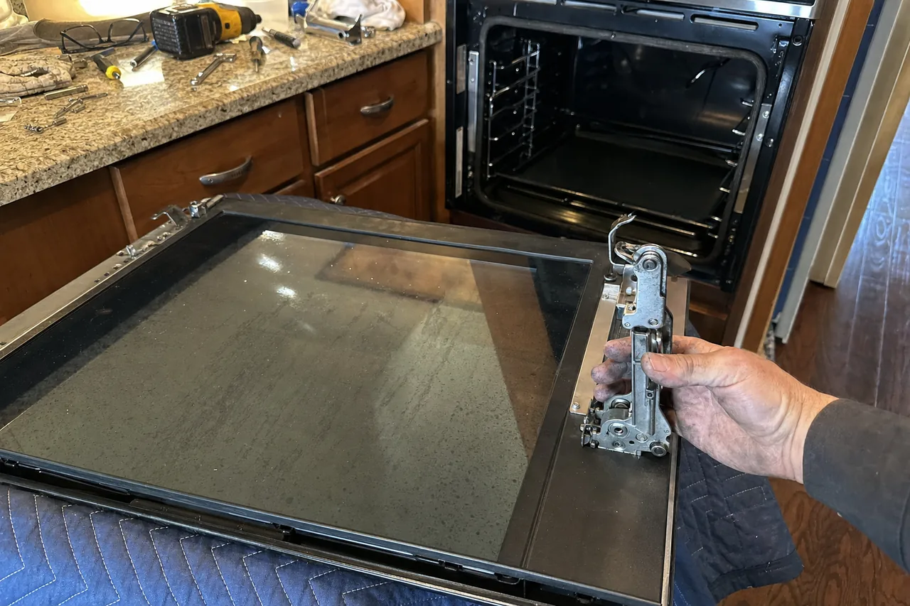 An empty built-in oven cavity with its door removed, tools laid out on the granite counter beyond