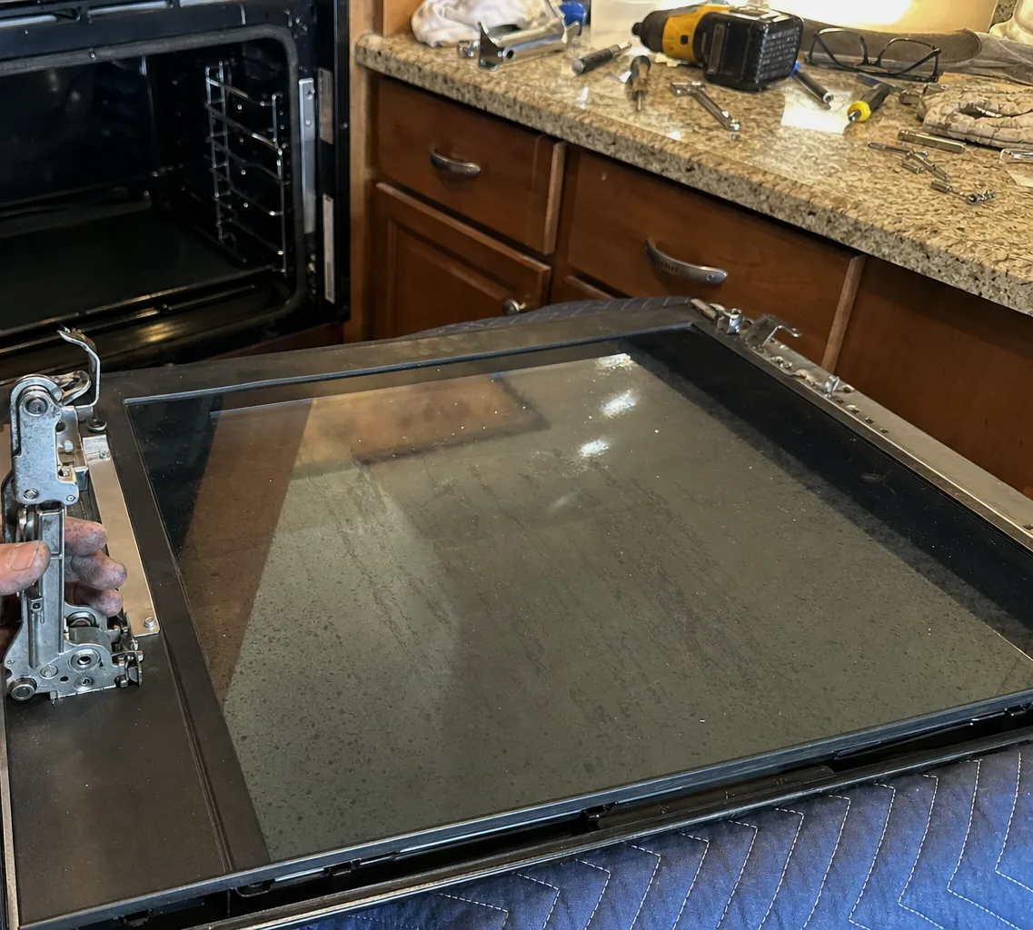 A stripped oven door and a hand on its hinge, seen from above with the kitchen floor beneath