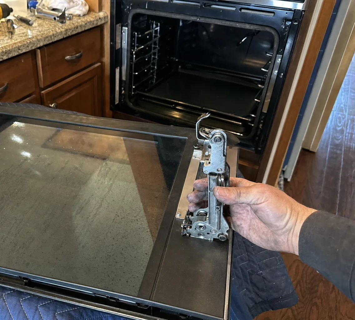 Hand tools and hinge hardware laid out on a granite counter above an open appliance cavity